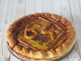 Round open home celebratory apple, bathed in beaten eggs, pie with numbers 64 for birthday on a wooden white table.A modest home celebration with a pie.