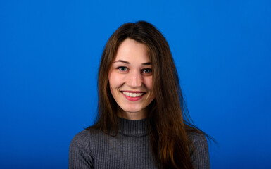 Fototapeta premium Photo of smiling, cheerful young female in grey dress on blue background