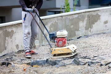 A construction worker compacts crushed stone with a petrol vibratory compactor.