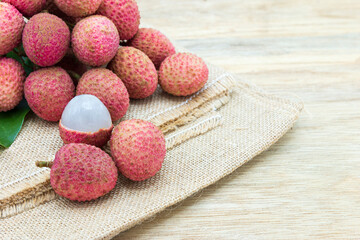 Pile of fresh lychee sweet fruit and peeled showing white fleshon on hemp sacks and wood background with copy space, Tropical fruits in thailand.