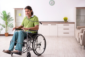 Young male invalid in wheel-chair suffering at home