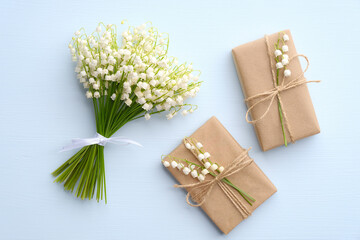 Bouquet of flowers lily of the valley and two gift boxes wrapped kraft paper on blue table, view...