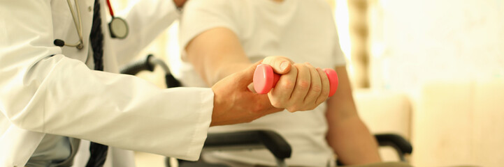 Handicapped man sits working out dumbbell arm. Rehabilitation after injuries. Treatment and...