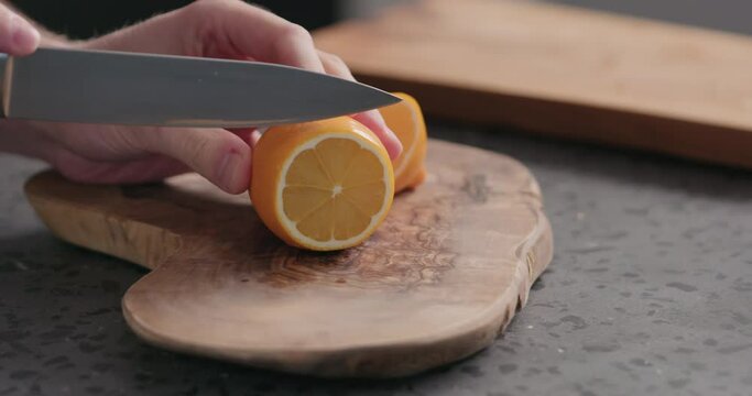 Slow motion man slicing fresh orange lemon on olive board