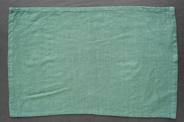 Crumpled linen fabric on black slate stone wooden background, top view