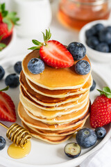 American pancakes with berries and honey on a white plate. Stack of fritters with strawberries and blueberries. Tasty healthy breakfast. Selective focus