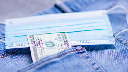 Dollar bill sticking out from a blue jeans pocket. American banknote and medical mask. Business medical concept