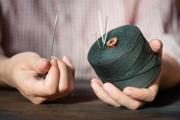 Sewing thread spool and needle in tailor hand close up.