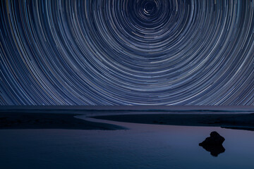 Digital composite image of star trails around Polaris with Vibrant landscape of low tide beach