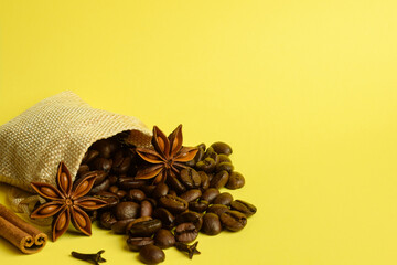Coffee grains scattered from a small bag lie with anise and cinnamon