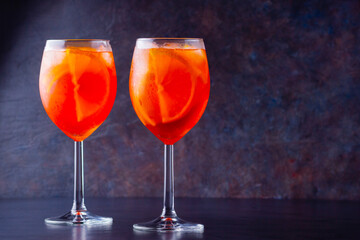 Aperol spritz cocktail in glass on dark background. Two glasses of aperol spritz with sliced orange. Summer cocktail in glass. Copy space