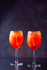 Aperol spritz cocktail in glass on dark background. Two glasses of aperol spritz with sliced orange. Summer cocktail in glass. Copy space