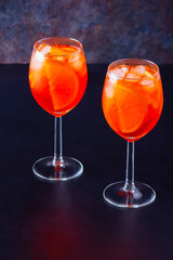 Aperol spritz cocktail in glass on dark background. Two glasses of aperol spritz with sliced orange. Summer cocktail in glass. Copy space