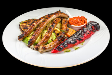 Delicious grilled handmade sliced sausage with bbq vegetables on a white plate, isolated on black background