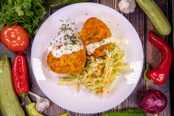 Delicious potatoes balls garnish with cabbage, dill and sauce in a plate on a wooden table, top view