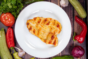 Delicious grilled chicken breast on a white plate, on a wooden table. Top view