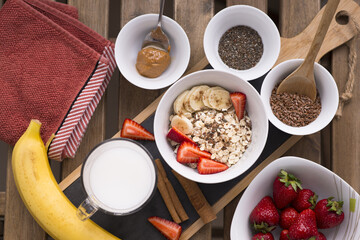 Healthy breakfast with bowl of oatmeal, flaxseed, chia seeds, strawberries,banana, cinnamon sticks and peanut butter on wooden table