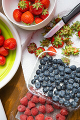Fresh strawberries in a sieve and a cup being cleaned, raspberries and blueberries in a plastic cup beside it