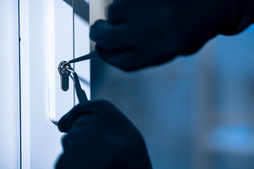 Robber in black balaclava cracking door with metal picklock