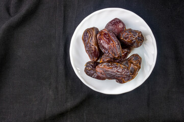 Big luxury dried date fruit in bowls on the dark surface, kurma ramadan kareem concept, close up.