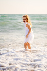 girl in white dress walks and fun on sea shore with big waves and strong winds.