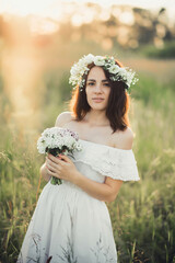 beautiful young girl with a bouquet of flowers and a wreath in a white dress