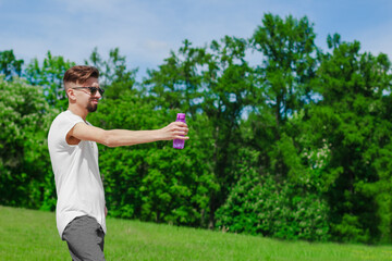 Young sporty man in sun glasses standing with a bottle of water from eco plastic green grass on the background.  Concept of sport, outdoors activity, rest, health care, environmental protection.