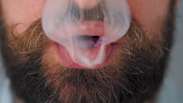 Close-up of a bearded man's mouth chewing chewing gum. Man blowing out a bubble of bubble gum