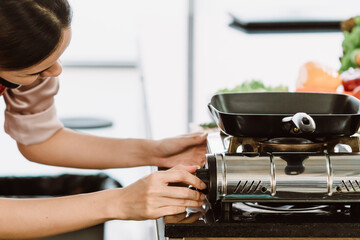 Asian female chef dressed in an apron cooking in the kitchen are turning on the gas stove to cook in a modern style kitchen.