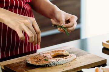 Asian Cook Is sprinkling herb on raw salmon To prepare food on the modern kitchen counter