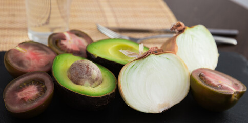 vegetables black tomatoes, avocado and onions on black stone board