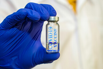 vial with the vaccine in the hands of a doctor in blue protective surgical gloves inscription on the vial COVID19 vaccine doctor in the background in blur