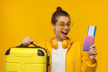 Young excited girl ready for travelling, holding passport with airplane tickets and suitcase for...