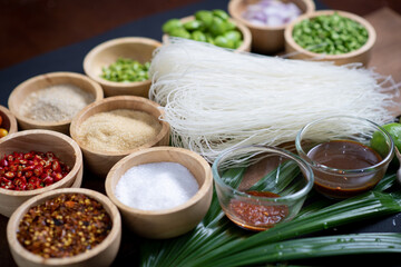 Raw rice flour in a wooden bowl with spices On a dark wood with natural light, focusing on the top of the noodles
