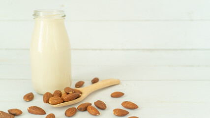 Almond milk in a bottle with almonds in a wooden scoop on white wood background with copy space. Alternative milk concept.