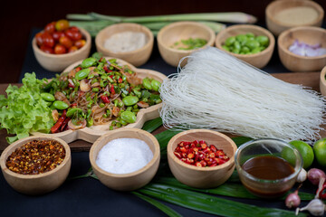 Raw rice flour in a wooden bowl with spices On a dark wood with natural light, focusing on the top of the noodles