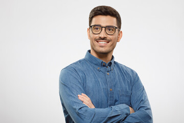 Portrait of young handsome smiling man dressed in shirt and eyeglasses, standing with arms crossed,...