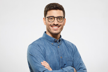 Young handsome business man wearing blue shirt and eyeglasses, holding arms crossed, smiling and feeling confident, isolated on gray background