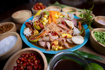 Raw rice flour in a wooden bowl with spices On a dark wood with natural light, focusing on the top of the noodles