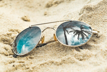 Mirrored sunglasses close up on the beach sand with palm trees reflection