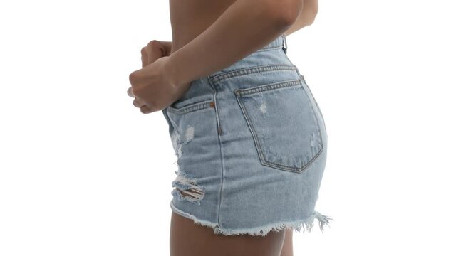 Side view of young beautiful African woman unbuttoning and taking off sexy torn denim shorts. Isolated, on white background