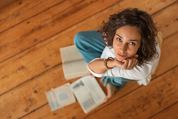 A curly-haired girl with books is sitting on the wooden floor. Distance learning