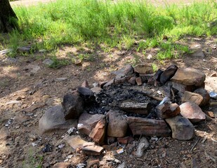 Embers left from a bonfire in a campsite, with green grass in the background