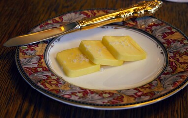 Three slices of butter with a golden knife in a round white plate with printed border