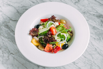 Vegetarian tomato, olives pepper salad in a white plate on a marble table, healthy food