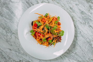 Vegetarian tomato, olives pepper salad in a white plate on a marble table, healthy food