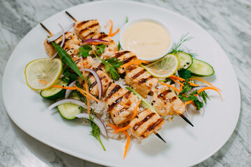 chicken kebabs with rice in a white plate on a marble table