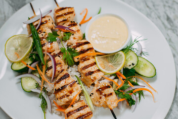 chicken kebabs with rice in a white plate on a marble table