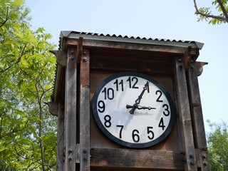 Fototapeta na wymiar White round wall clock with black Roman numerals and borders, mounted on a wooden crate in a park