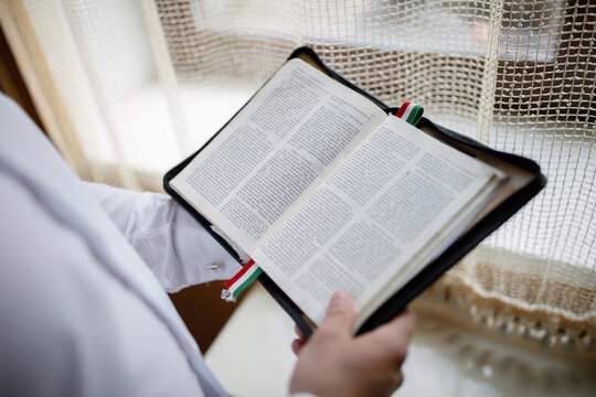 a man near the window is reading and holding a bible in Hungarian. priest prepare for service in the church.